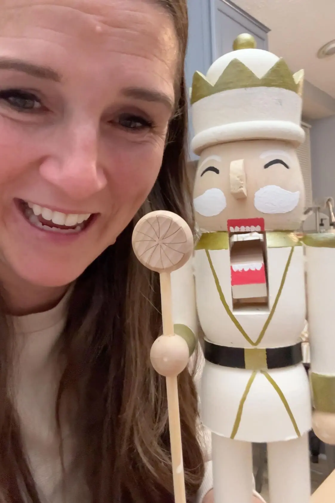 Smiling woman posing with her completed nutcracker, which has a white face, black and gold outfit, and a staff. The joy of crafting is evident in her expression, making the nutcracker look like a cherished holiday decoration.